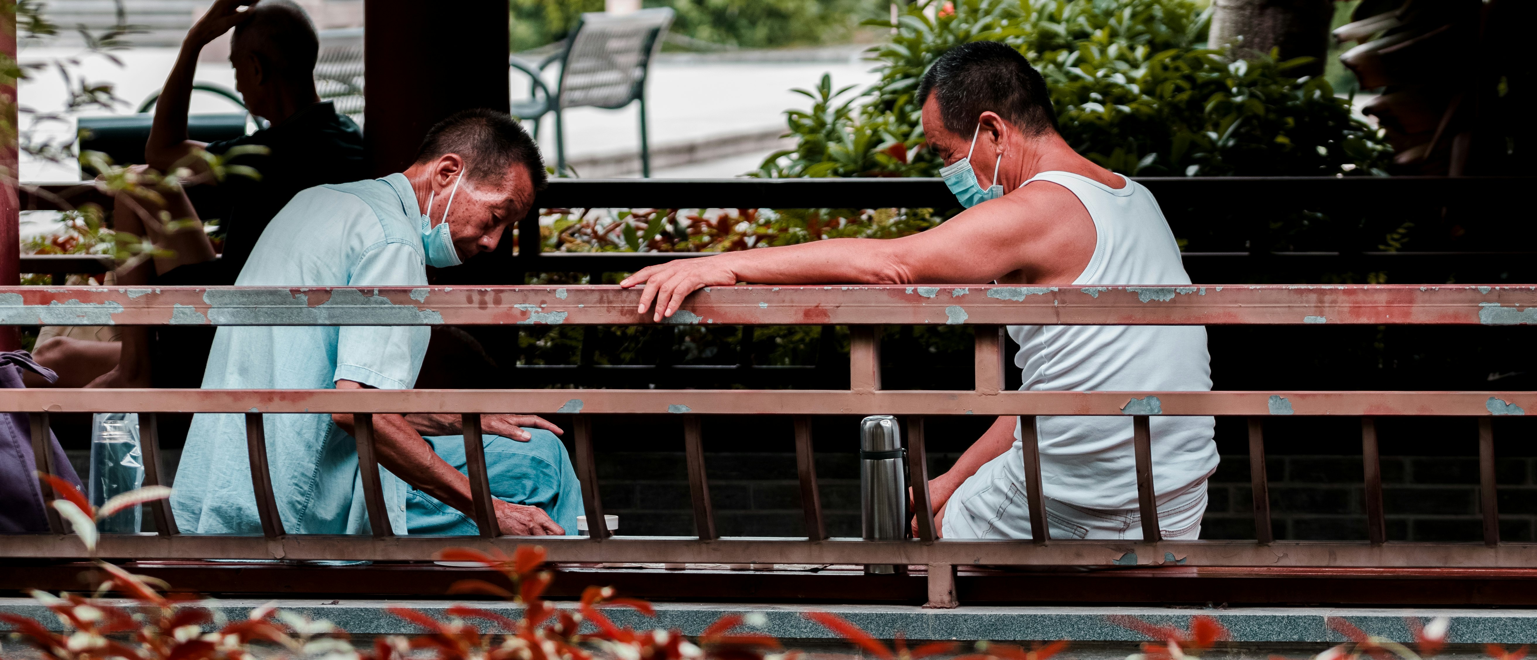 man in white tank top sitting on brown wooden bench during daytime